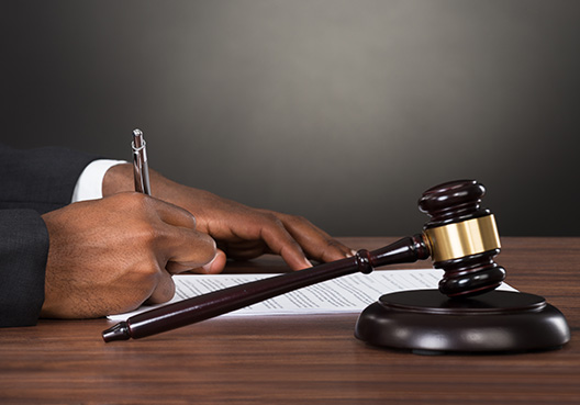 A man sitting behind desk signing document with gavel beside him