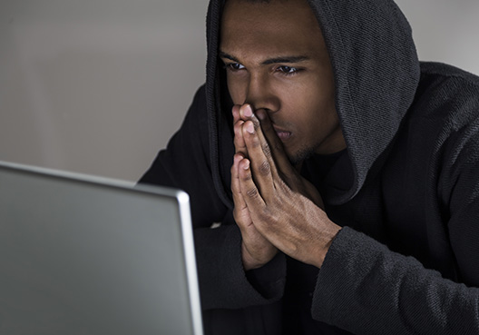 man holding his hands to his face in a prayer-like state while watching his laptop