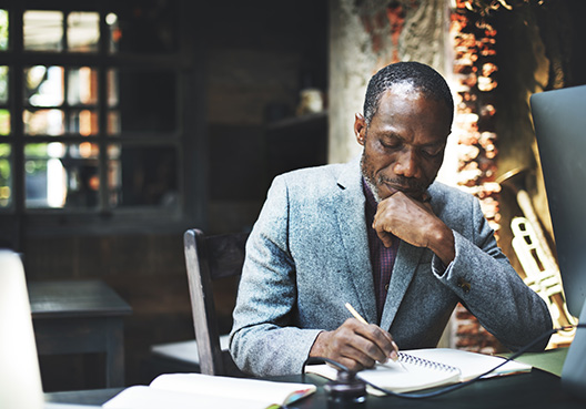 man writing in a book by his desk